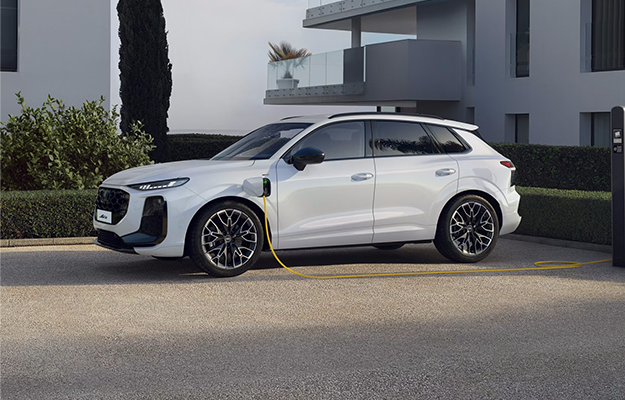 Ein weißer Audi Q3 steht an einer Ladesäule vor einem Wohnhaus